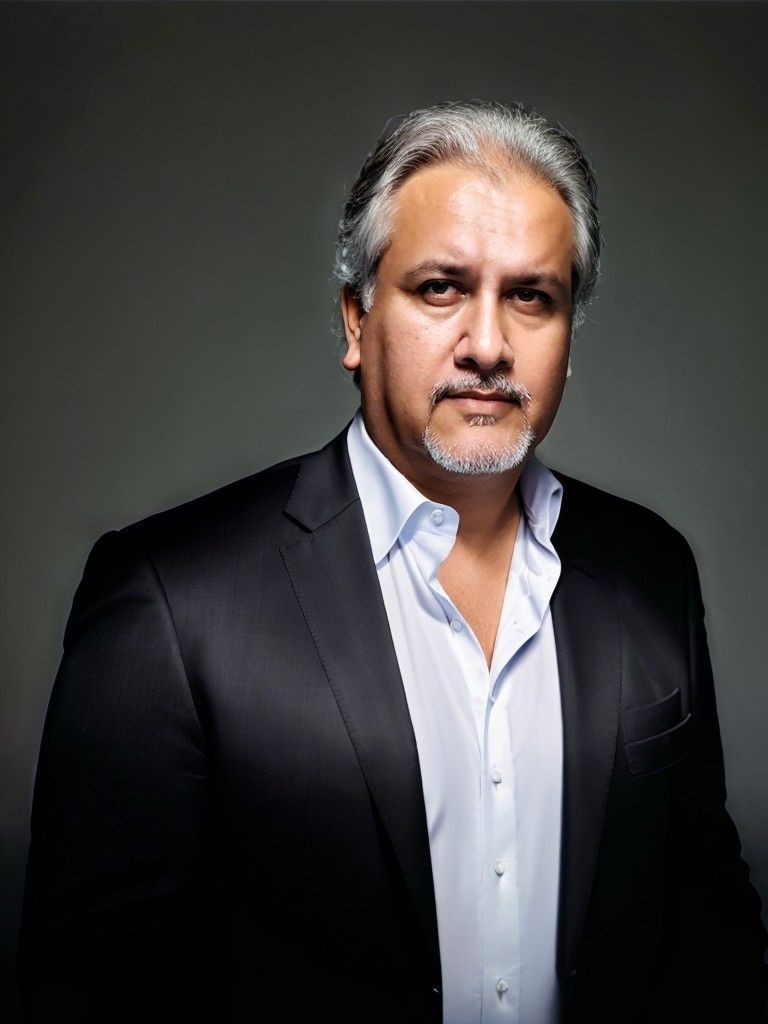 Close-up of a man wearing a black suit and white dress shirt with a dark background.