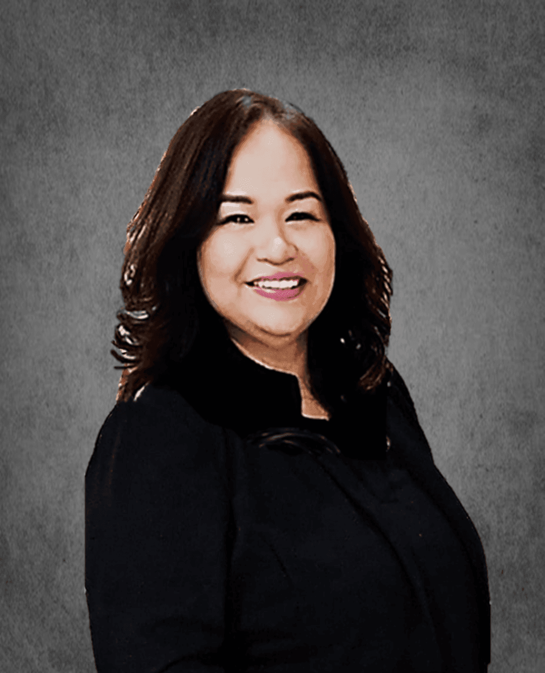 Individual with long, wavy brown hair wearing a dark, formal outfit against a gray background.