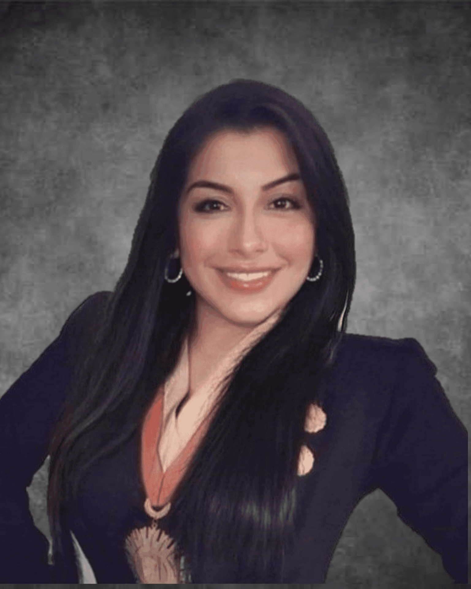 Smiling woman with long dark hair in a black blazer against a gray background.
