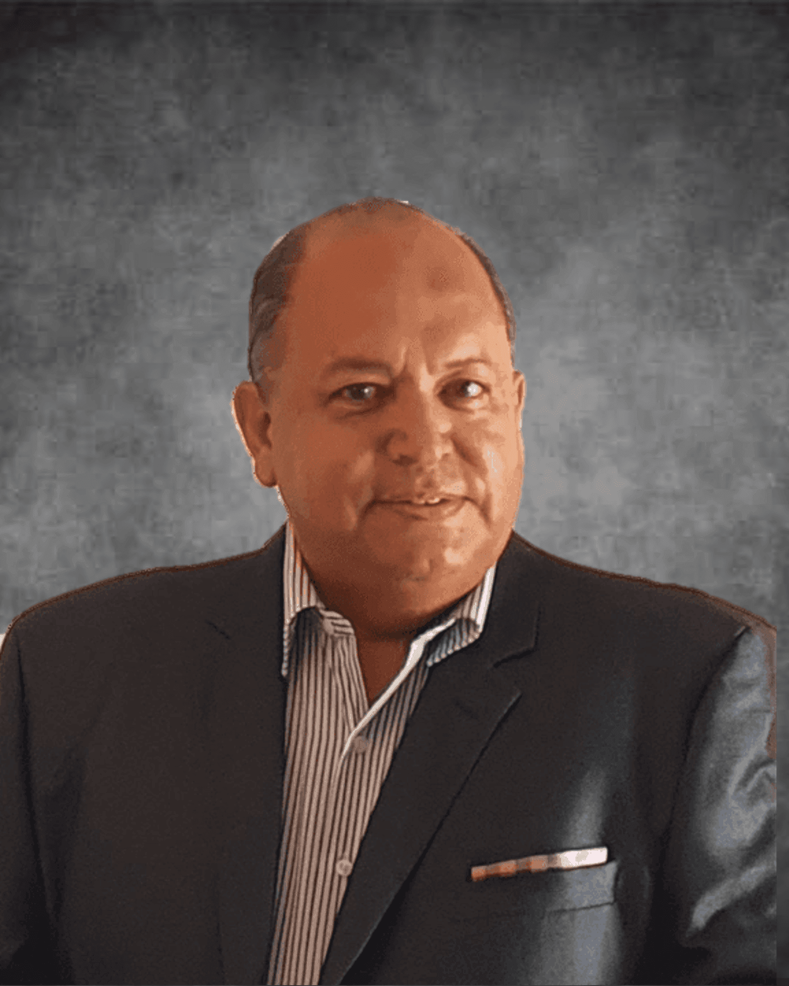 Person wearing a dark suit jacket over a striped collared shirt, standing against a grey background.