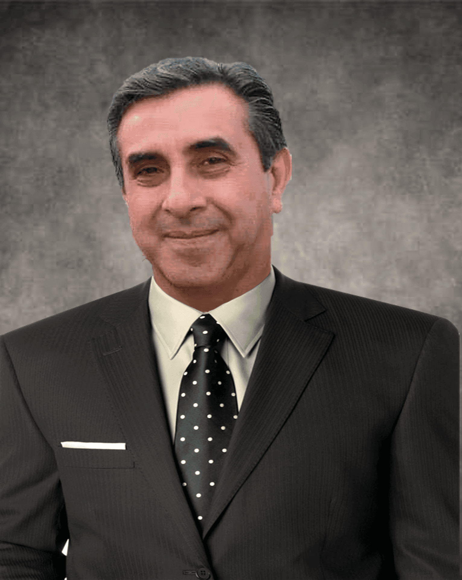Smiling man in a dark suit with polka dot tie against a gray background.