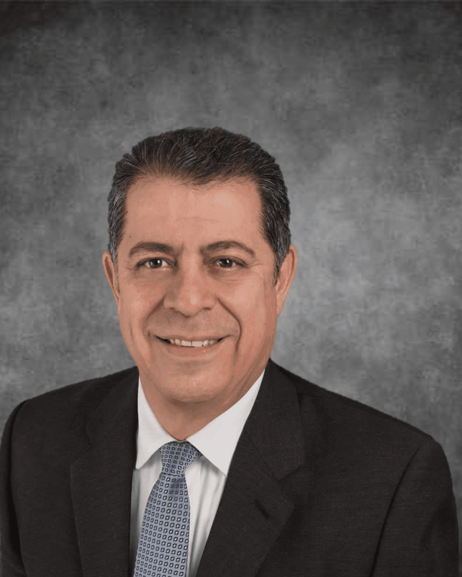 Man in a business suit with a blue tie, standing against a gray textured background.