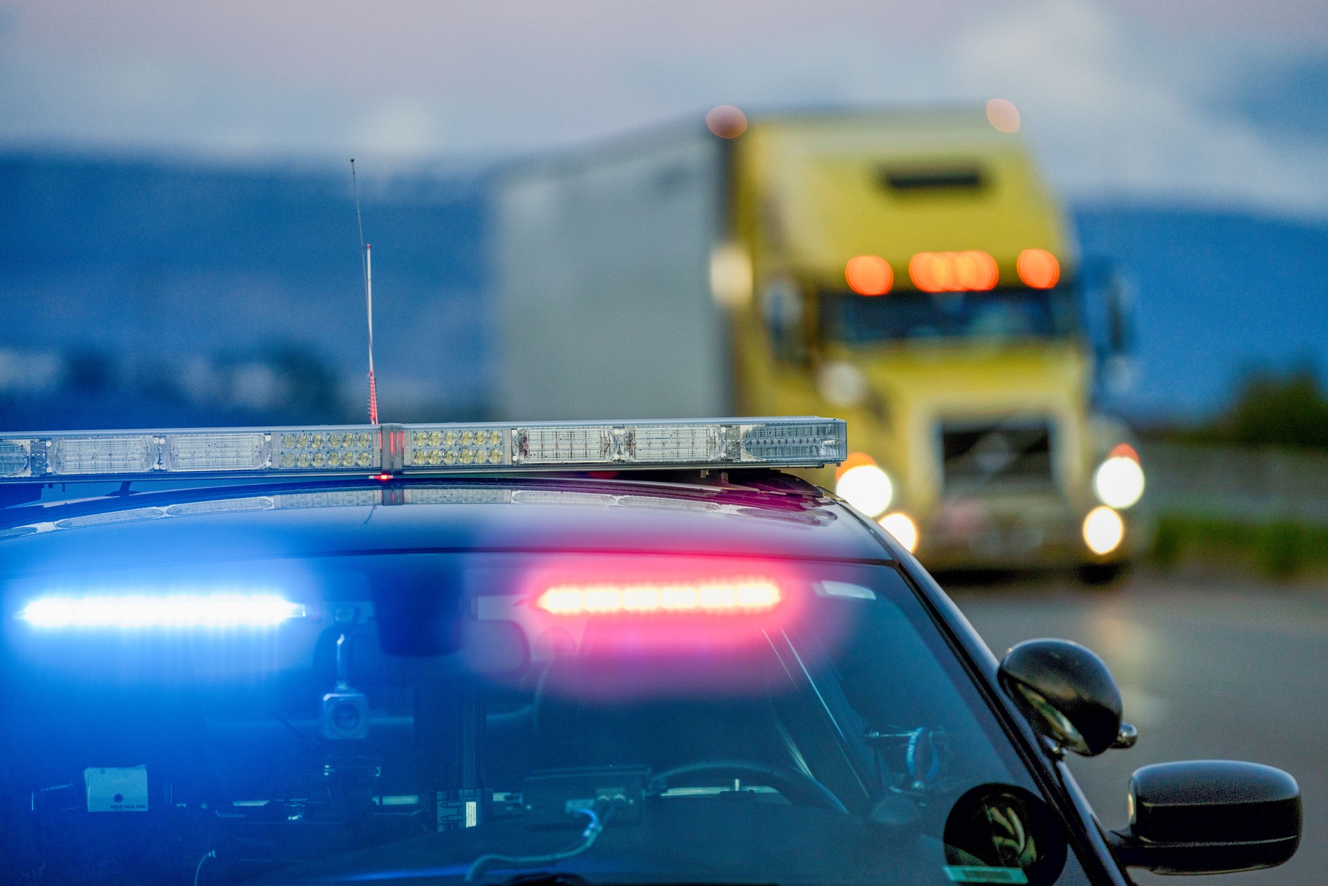 A Highway Patrol Car With The Lights On, Pulling A Driver Over For Speeding As A Semi Truck Drives Passed